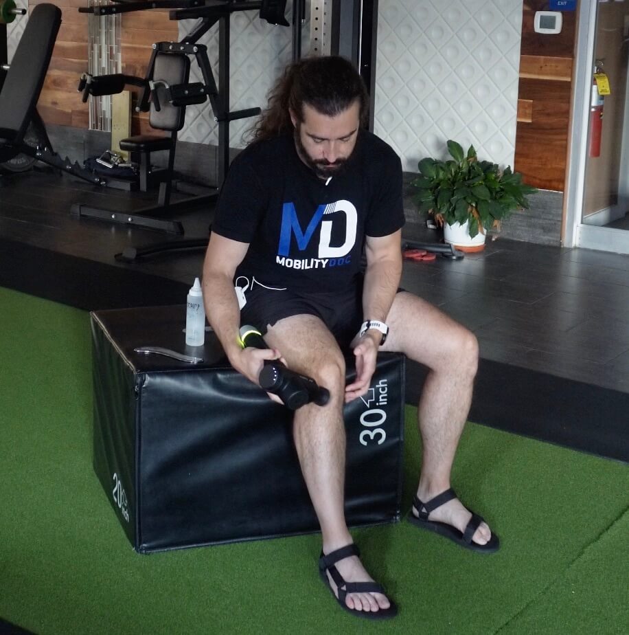 Dr. John using a massage gun to help warm up his knee before muscle scraping for knee pain